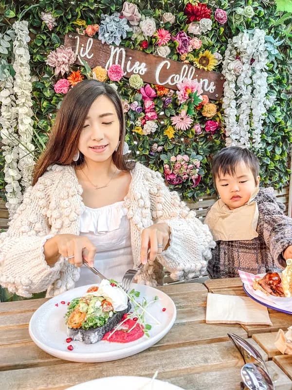Jeannie and her toddler dining in front of a floral wall at an event