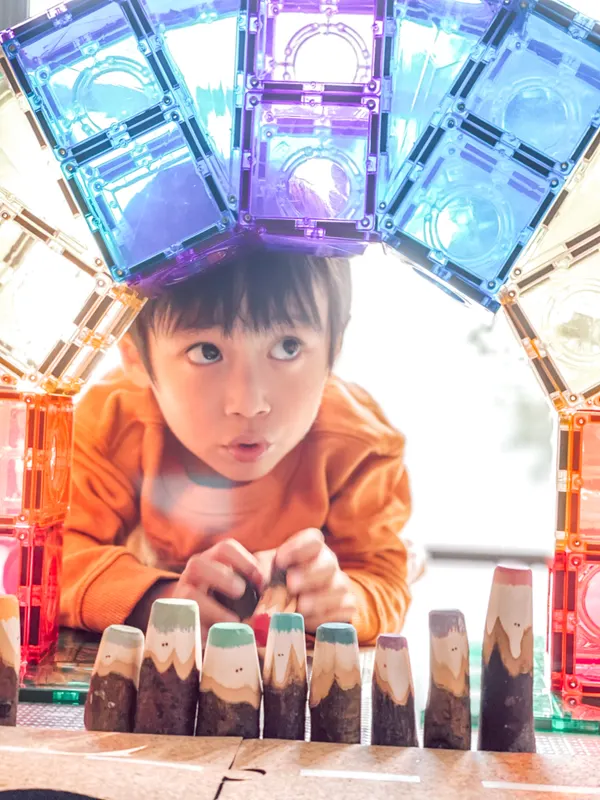 A young boy peeking through a colourful arch of magnetic building tiles