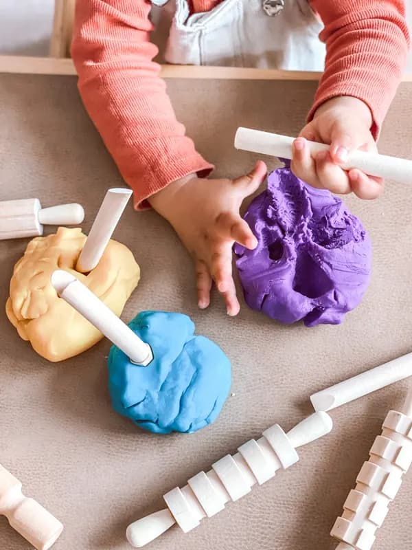 Small hands shaping colourful playdough with rolling tools