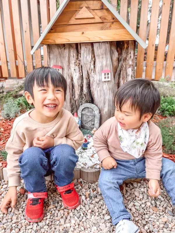 Two young brothers laughing together on garden pebbles beside a fairy door