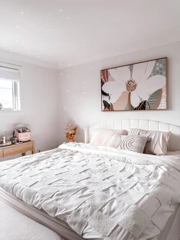 A calm white bedroom with a botanical artwork above the bed