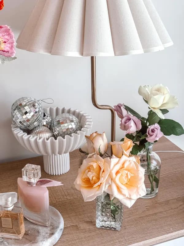 A pleated lamp, disco-ball ornaments and peach roses on a bedside table