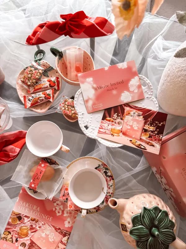 A red and pink sakura-themed gift set spread out with tea cups and sweets